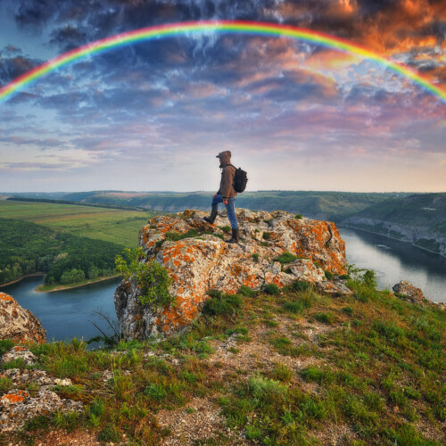 空に虹と岸壁に立つ人の写真